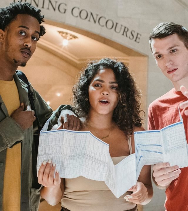 Amazed young multiracial male and female friends in casual outfits looking away while exploring map in Grand Central Terminal